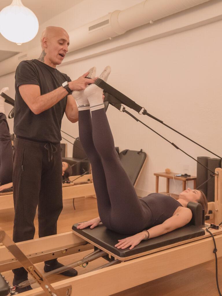 Instructor de pilates ajustando postura de alumna en reformer
